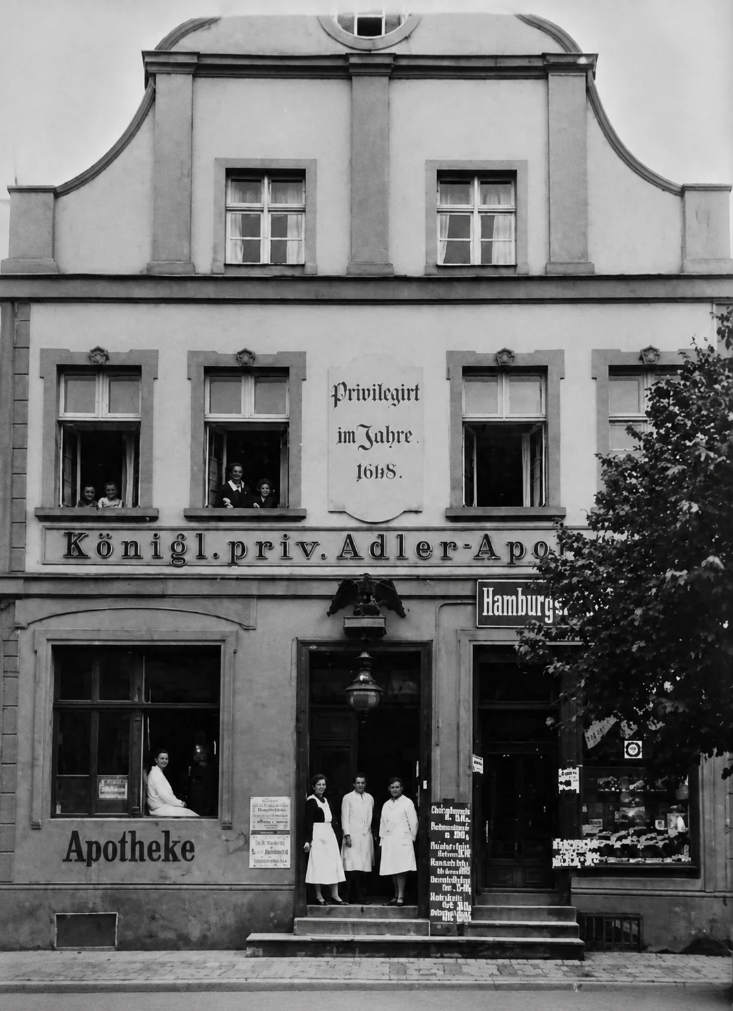 Archiwalna fotografia fasady apteki z personelem w białych fartuchach przed wejściem
